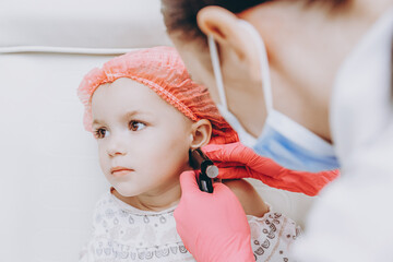 The process of piercing a child's ears in a beauty salon with a piercing gun. Portrait of a girl in...