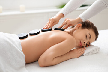 Obraz na płótnie Canvas Young lady receiving hot stone massage at modern spa