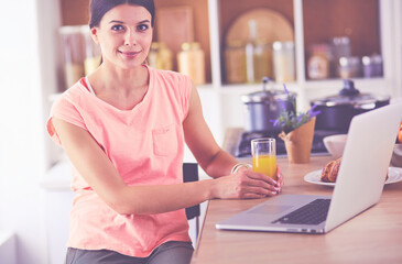 Young woman in kitchen with laptop computer looking recipes, smiling. Food blogger concept