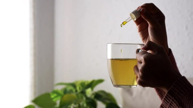 Alternative medicine - Hand dripping cbd oil to cup of tea - Biologic and organic hemp herbal plant