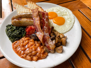 Breakfast with Cumberland sausages, fried eggs sunny side up, sautéed mushrooms , spinach, crispy bacon, grilled tomatoes, baked beans and toasted bread. 