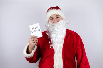 Man dressed as Santa Claus standing over isolated white background holding a notebook with a merry christmas message