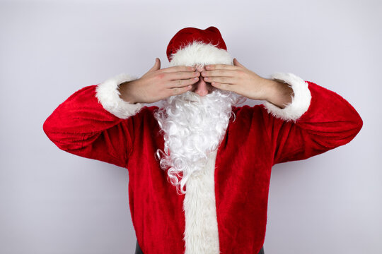 vMan dressed as Santa Claus standing over isolated white background covering eyes with hands smiling cheerful and funny. Blind concept.