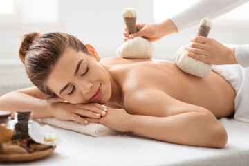 Masseuse making body massage with herbal compress balls