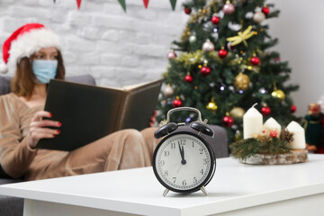 Bored young woman in Santa hat alone at home on New Years Eve, reading a book. Winter holidays during Corona virus outbreak, self-quarantine concept.