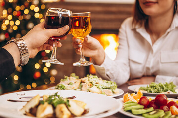 loving couple celebrating Christmas or New Year's Eve at home at a holiday table, drinking wine and greeting each other with a holiday