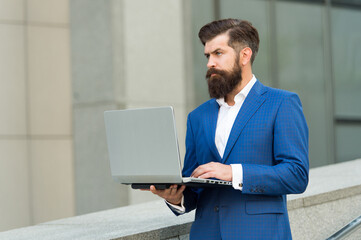 Brutal businessman in formal business suit use laptop for working online outdoors, e-business