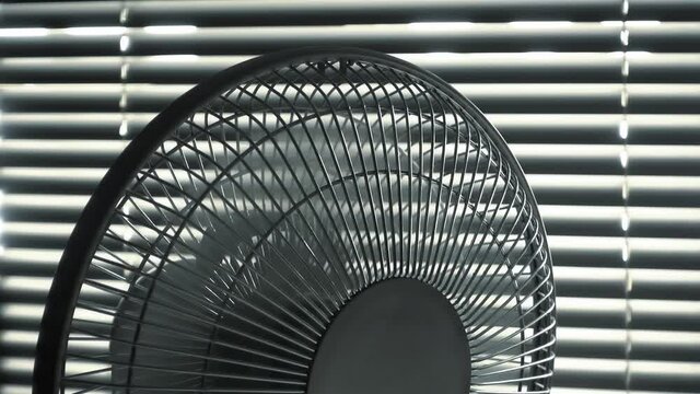 Close up of electric home fan or ventilator running in front of metallic blinds