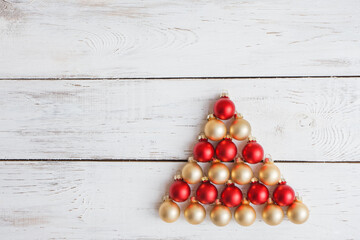 Christmas balls in red and gold on a white wooden background in the shape of a Christmas tree. Space for text. The concept of the celebration.