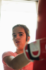 joven adolescente practica deporte boxeo con guantes y bolsa para golpes en habitación de...