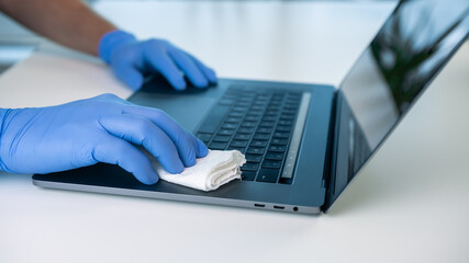Person cleaning and disinfecting the laptop keyboard to prevent the coronavirus.