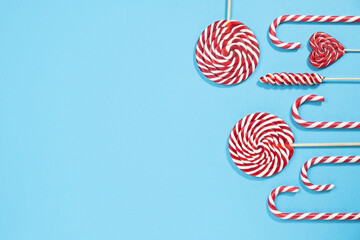 Fototapeta na wymiar Christmas red striped candy canes and lollipops on blue background. Merry Christmas sweets and Happy New Year concept. Flatlay, copy space