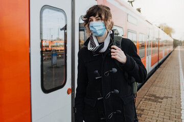 Fototapeta na wymiar Coronavirus, COVID-19. Young german woman with medical face mask to protect against the coronavirus while waiting for the train on the subway platform. Mouth protection obligation at the train station