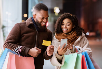 Portrait of happy afro couple using smartphone holding credit card