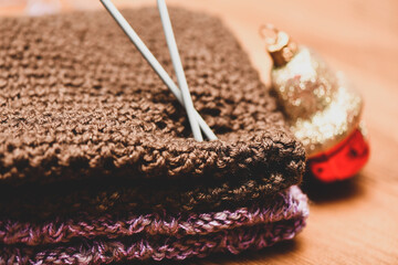Winter knitted scarf, knitting needles and New Year decorations. Festive home atmosphere with Christmas toys and shiny glitters.