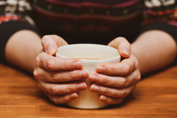Young woman holding hot cocoa or coffee cup. Autumn or winter moody weekend, New Year, and Christmas background. Lazy day, quarantine, stay home, cozy scene, hygge concept.