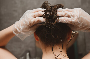 A young woman puts a healing mask on her hair at home. The girl coloring her hair in her own bathroom. Self-care and lifestyle, solving hair issues.