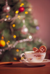 Gingerbread man cookie in a coffee mug in front of decorated Christmas tree. Christmas scene with sweet gingerbread cookie.