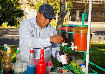 Hispanic street seller in a colorful food cart preparing sweet ice desserts 
