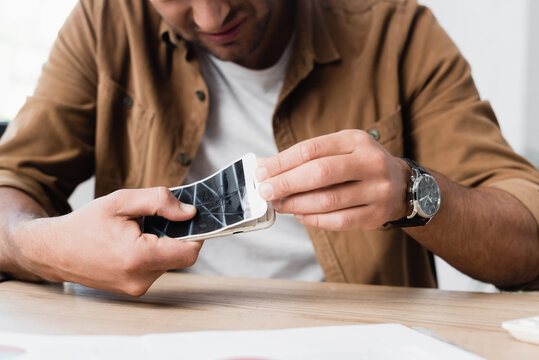 Cropped view of businessman disassemble smashed smartphone while sitting at table on blurred foreground