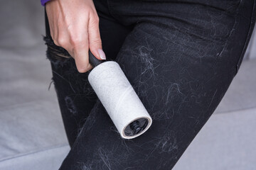 Woman cleans clothes with clothes roller, lint roller or sticky roller. Cleaning pets hair on the...
