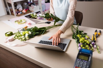 cropped view of florist using laptop near payment terminal and eustoma flowers on table