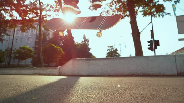 SLOW MOTION TIME WARP, LENS FLARE, CLOSE UP, LOW ANGLE, DOF: Skateboarder lands a nollie kickflip during freestyle session at an urban skate park. Unrecognizable man lands a trick while skateboarding