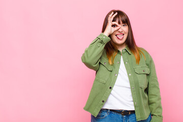 overweight woman smiling happily with funny face, joking and looking through peephole, spying on...