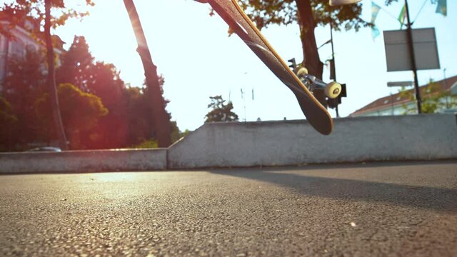 SLOW MOTION TIME WARP, LENS FLARE, LOW ANGLE, CLOSE UP, DOF: Unrecognizable skateboarder lands a 360 flip during a freestyle session in the sunlit park. Young skater successfully lands a flip trick.