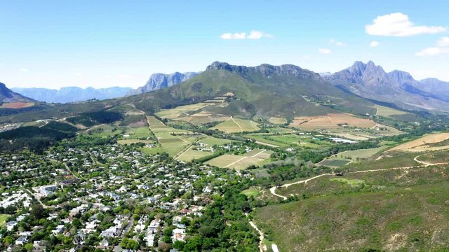 Aerial of suburban neighbourhood and farms in green valley between mountains, Stellenbosch, Coetsenburg and Jonkershoek area