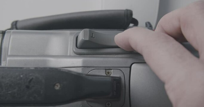 Caucasian hand pushing zoom control on old mini dv camera. Static shot with soft light.