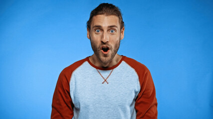 shocked young man with open mouth looking at camera on blue
