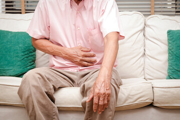 Elderly men have abdominal pain sitting on the sofa in the house. Concept