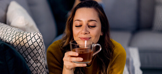 Young pretty woman drinks a cup of tea while lying on the couch - home shooting