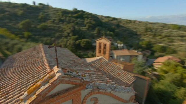 Fast aerial flyby close over cross on top of old church, with surrounding vineyards and hills in Tuscany, Italy.