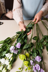 Obraz na płótnie Canvas partial view of florist holding eustoma flowers while arranging bouquet on blurred background