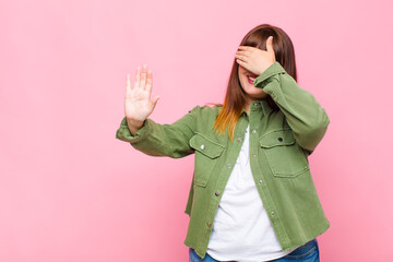 overweight woman covering face with hand and putting other hand up front to stop camera, refusing...
