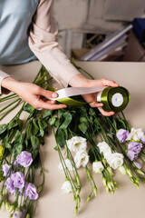 cropped view of florist holding decorative ribbon while making bouquet with eustoma flowers