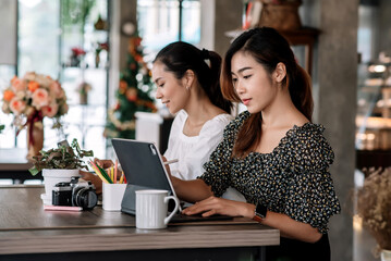 Two beautiful asian woman working together in a coffee shop with a digital tablet.