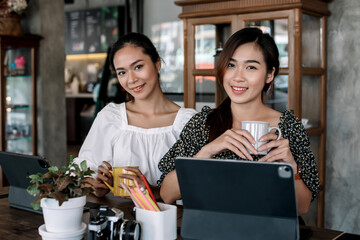 Two beautiful asian woman working together in a coffee shop with a digital tablet.