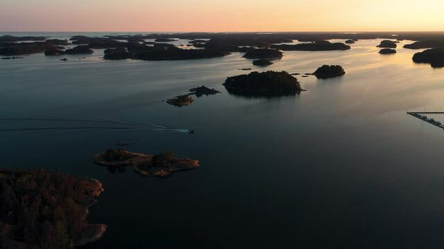 Aerial view following a motorboat driving between silhouette islands, serene, summer sunset, in the Stockholm archipelago, in Sweden- tracking, drone shot