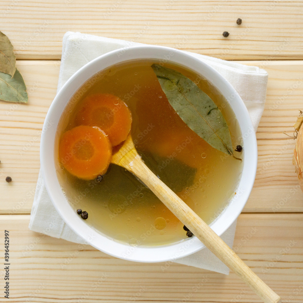 Wall mural Meat bone broth with vegetables and spices in white bowl on wooden background