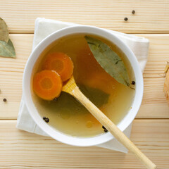 Meat bone broth with vegetables and spices in white bowl on wooden background