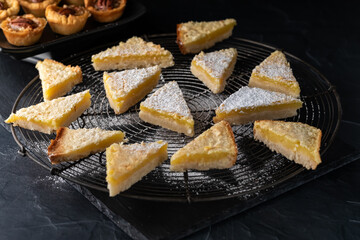 Lemon triangles with powdered sugar on a cooling rack and butter pecan tartlets in behind.