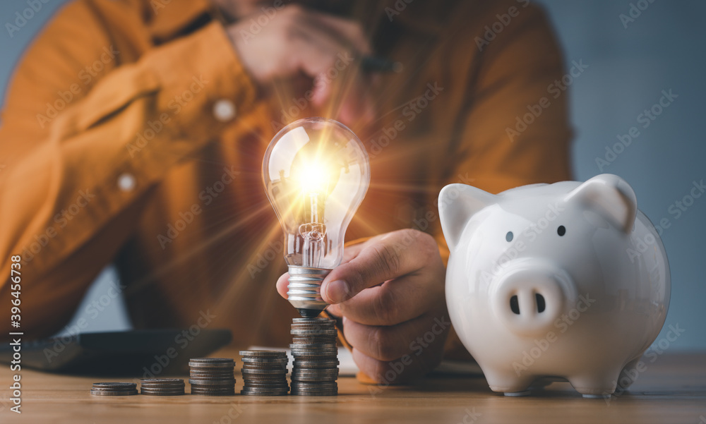 Poster saving energy and money concept. idea for save or investment. businessman holding lightbulb on piggy bank and coins stacking on desk with calculator.