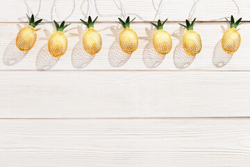 Christmas rustic background with string lights as pineapples golden colored on white wooden. Festive decoration, New Year fairy garland. Flat lay.