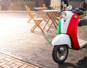 Vintage scooter coloured as Italian flag on sunny square near to street cafe. The concept of Italy vacation.