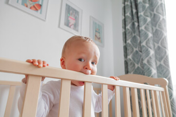 Blond cute little baby biting wooden bed headboard