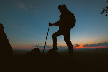 Silhouette of a man climbing a high cliff Climbers climb to the top enjoy the view A man watching the valley sunset in the evening