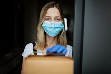 Cropped view of young waitress in latex gloves and protective face mask holding paper box package...
